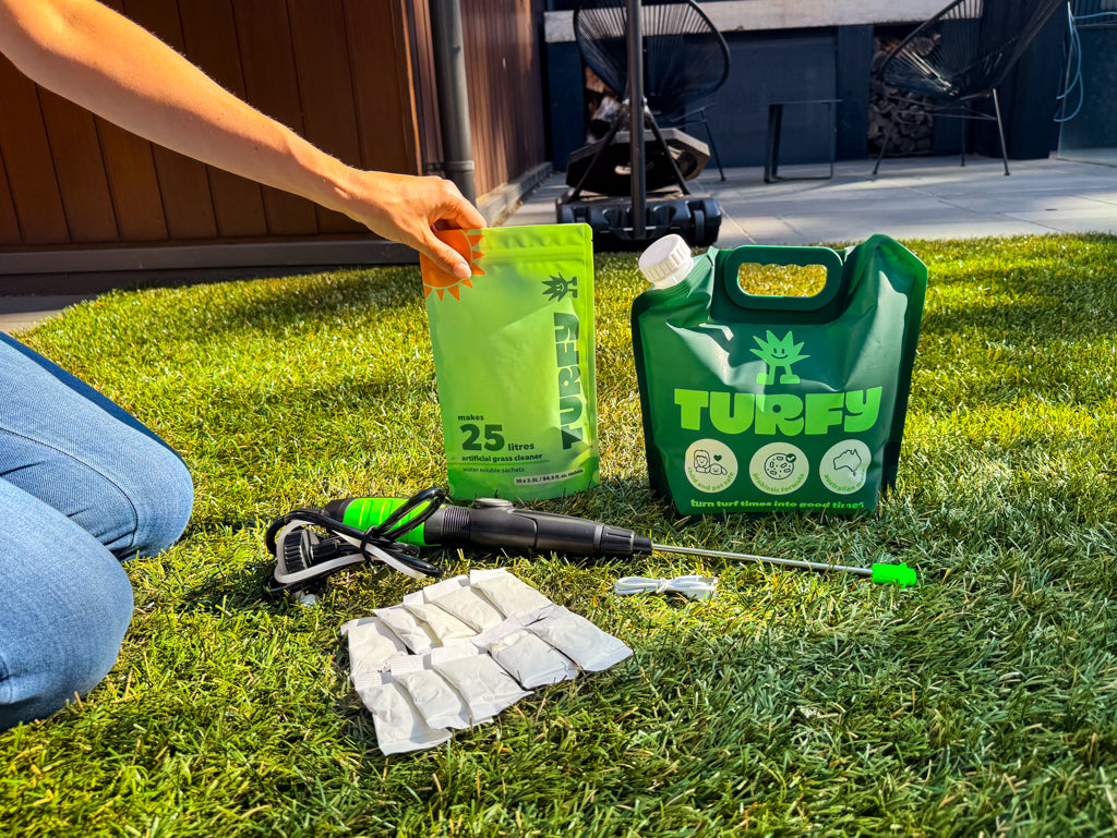 Turfy probiotic enzyme and bacteria artificial grass cleaning kit with female hand showing the probiotic refill packs, the 2.5L pouch and the battery sprayer.