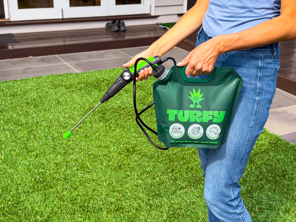 Woman holding the Turfy 2.5 litre battery sprayer kit with probiotic enzymatic cleaning solution spraying on large area of fake grass with pet urine. 